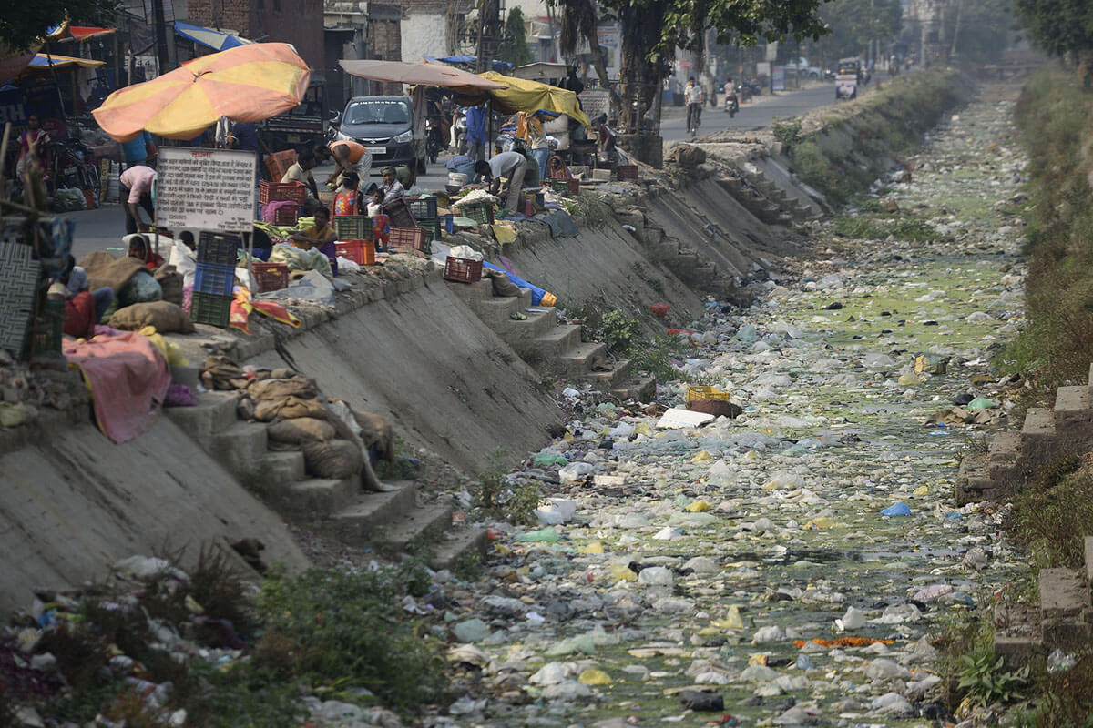 Pemilik warung di India duduk di samping kanal kering yang penuh dengan kantong plastik dan sampah di Jalandhar, 10 Mei 2018